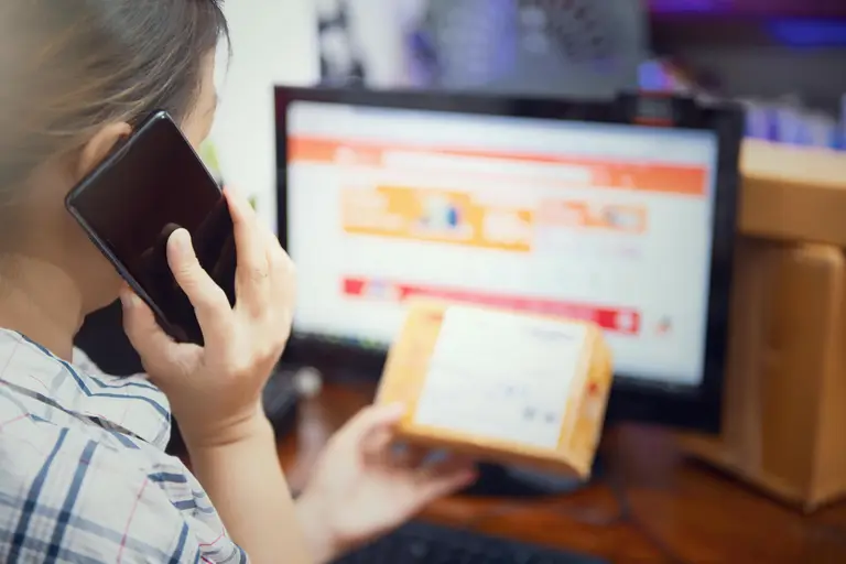 Femme parlant au téléphone avec un colis à côté pour illustrer le suivi ou la livraison
